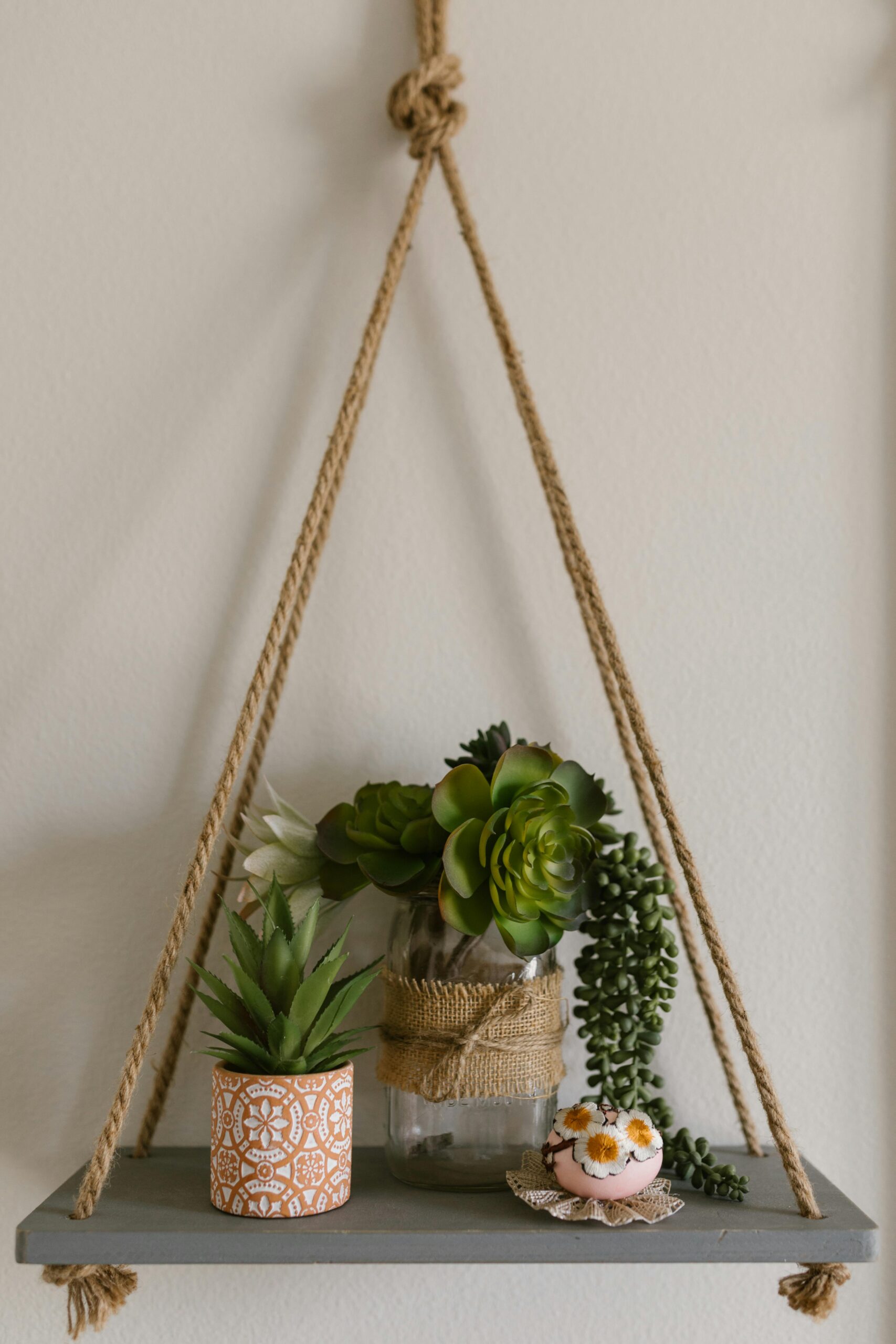 Stylowa wisząca półka linowa z sukulentami i przedmiotami dekoracyjnymi.