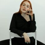 Ujęcie studyjne młodej rudowłosej kobiety siedzącej na krześle, emanującej elegancją i pewnością siebie.