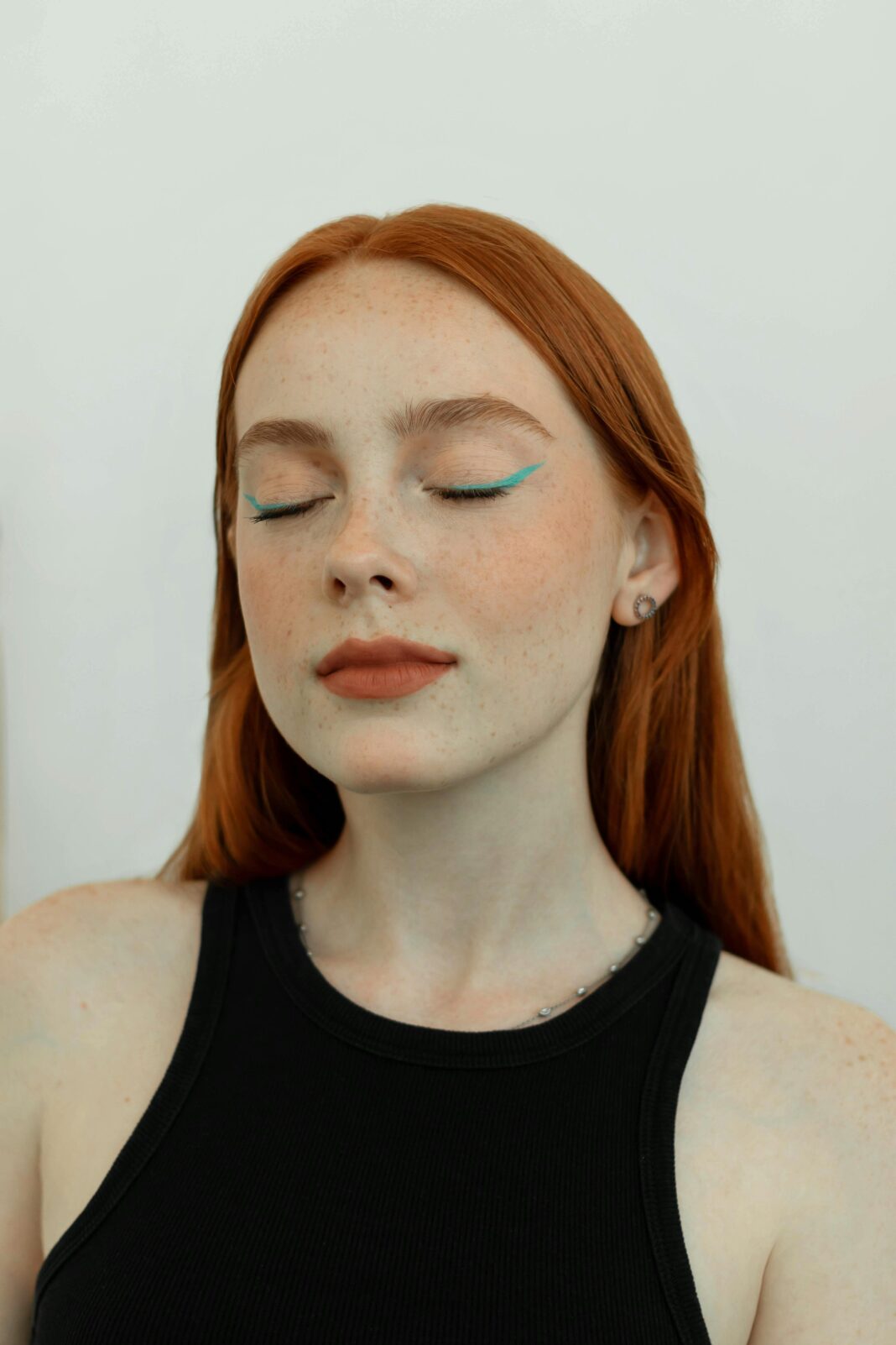 Wyrafinowany portret studyjny pięknej rudej kobiety z niebieskim eyelinerem i zamkniętymi oczami.