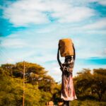 Młoda dziewczyna niesie kontener podczas spaceru po drodze w Turkana w Kenii podczas zachodu słońca.