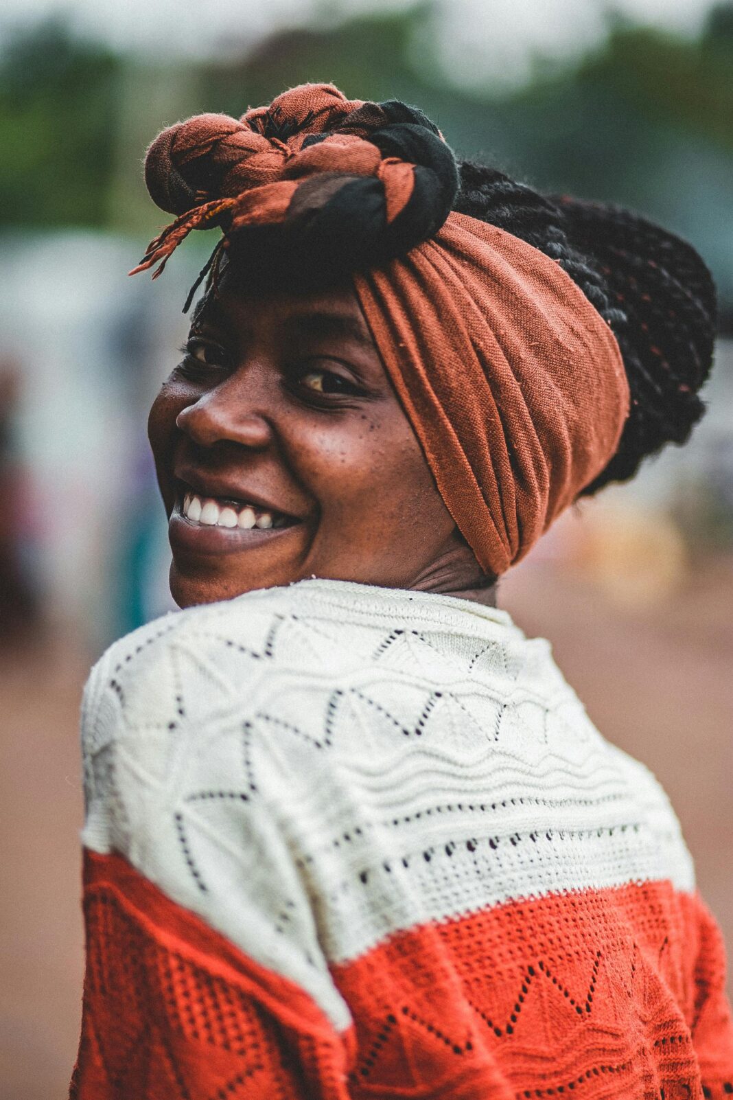 Radosna kobieta w chustce uśmiechnięta podczas sesji zdjęciowej w plenerze, promieniująca szczęściem.