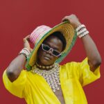 Najczęstsze błędy turystów w Kenii – jak ich uniknąć? Jasny i stylowy portret modnego mężczyzny w Nairobi w słomkowym kapeluszu na czerwonym tle.