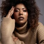 Zbliżony portret kobiety w wygodnym swetrze z golfem i efektowną kręconą fryzurą.