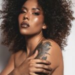 Oszałamiający portret eleganckiej kobiety z kręconymi włosami i kwiatowym tatuażem, ukazujący piękno i pewność siebie.