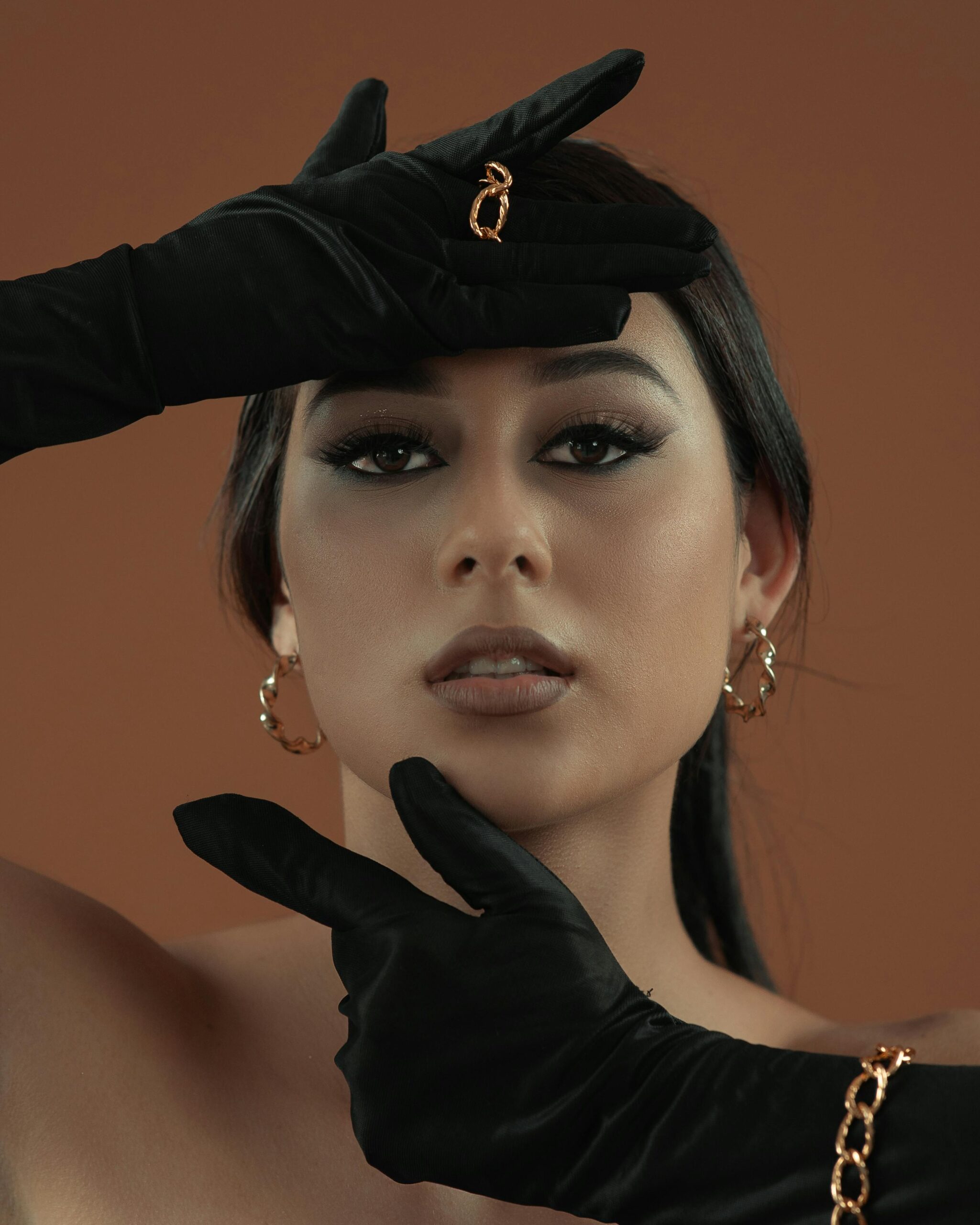 Wyrafinowany portret kobiety pozującej w czarnych rękawiczkach na brązowym tle.