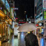 Osoba z parasolką spacerująca nocą po oświetlonych neonami ulicach Seulu w Korei Południowej.