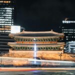 Jirisan: Najstarszy park narodowy Korei Nocny widok oświetlonej tradycyjnej bramy w miejskim pejzażu miejskim ze śladami świetlnymi o długim czasie ekspozycji.