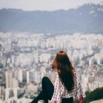 Kobieta siedząca na skale z widokiem na miejski krajobraz Seulu, Korea Południowa. 