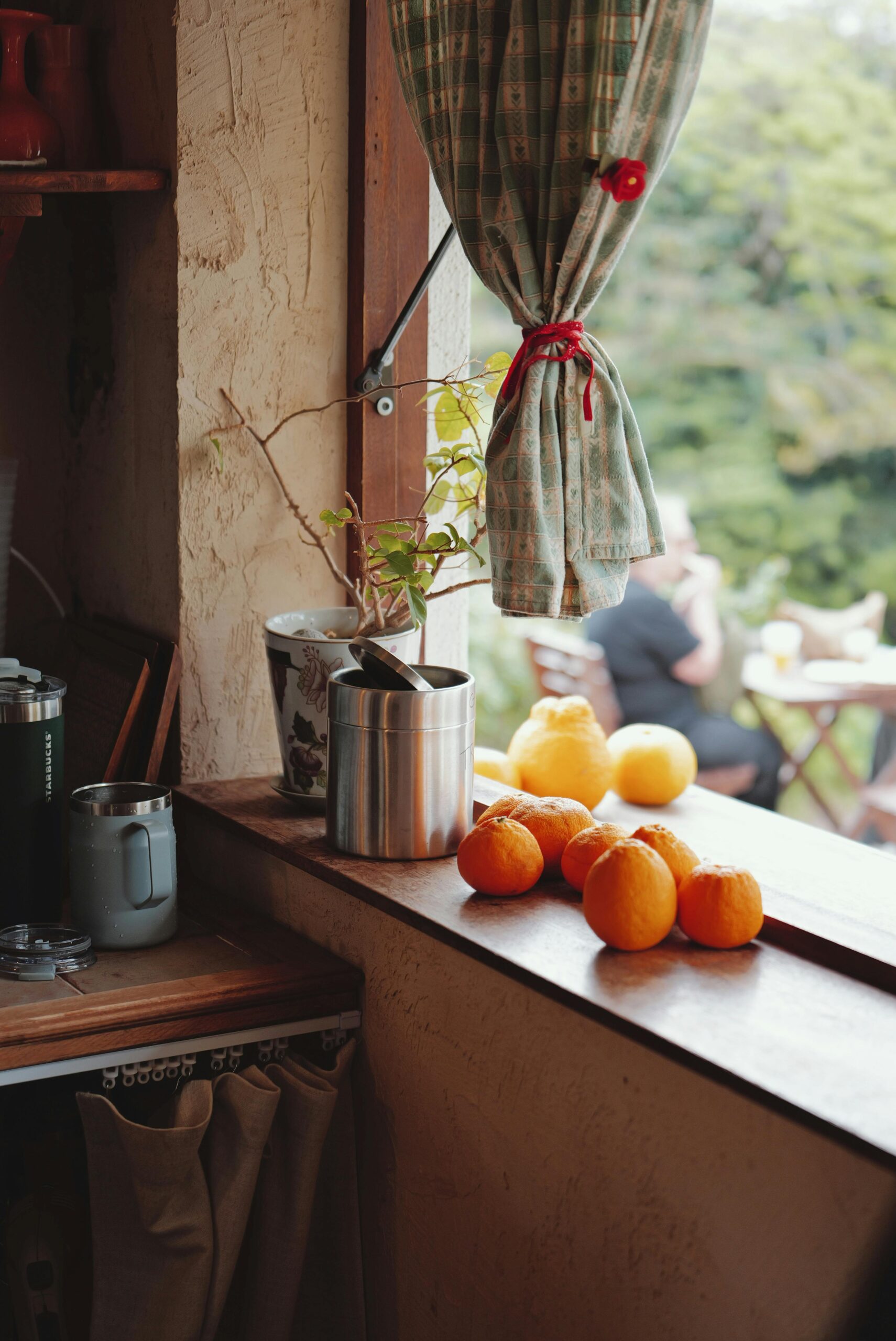 Ciepłe, rustykalne okno kuchenne z pomarańczami i widokiem na jadalnię na świeżym powietrzu, przywołujące przytulną, domową atmosferę.