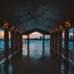 Drewniane molo z oświetlonymi światłami z widokiem na spokojny ocean o zachodzie słońca, idealne do podróży i tematów natury.
