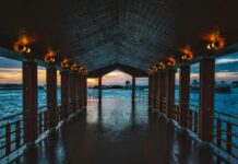 Drewniane molo z oświetlonymi światłami z widokiem na spokojny ocean o zachodzie słońca, idealne do podróży i tematów natury.