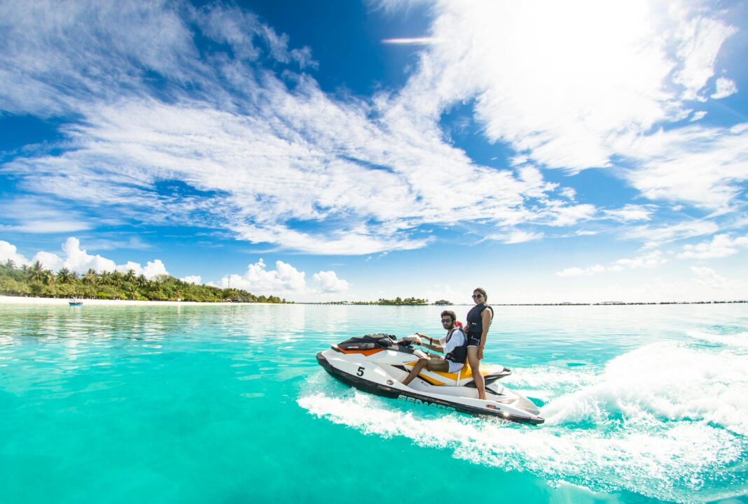 maldives Para ciesząca się ekscytującą przejażdżką skuterem wodnym po krystalicznie czystej wodzie pod jasnym niebem na Malediwach.