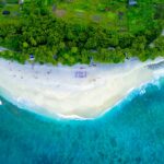Malediwy – jak wygląda życie codzienne mieszkańców atoli Zapierający dech w piersiach widok z lotu ptaka na tropikalną plażę na wyspie z bujną zielenią i turkusowymi wodami.