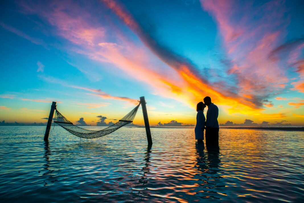 maldives Romantyczna para całuje się o zachodzie słońca przy tętniącym życiem niebie nad plażą na Malediwach.