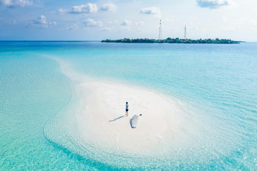 maldives Oszałamiający widok z lotu ptaka na samotną osobę na mierzei na Malediwach otoczoną turkusowymi wodami.