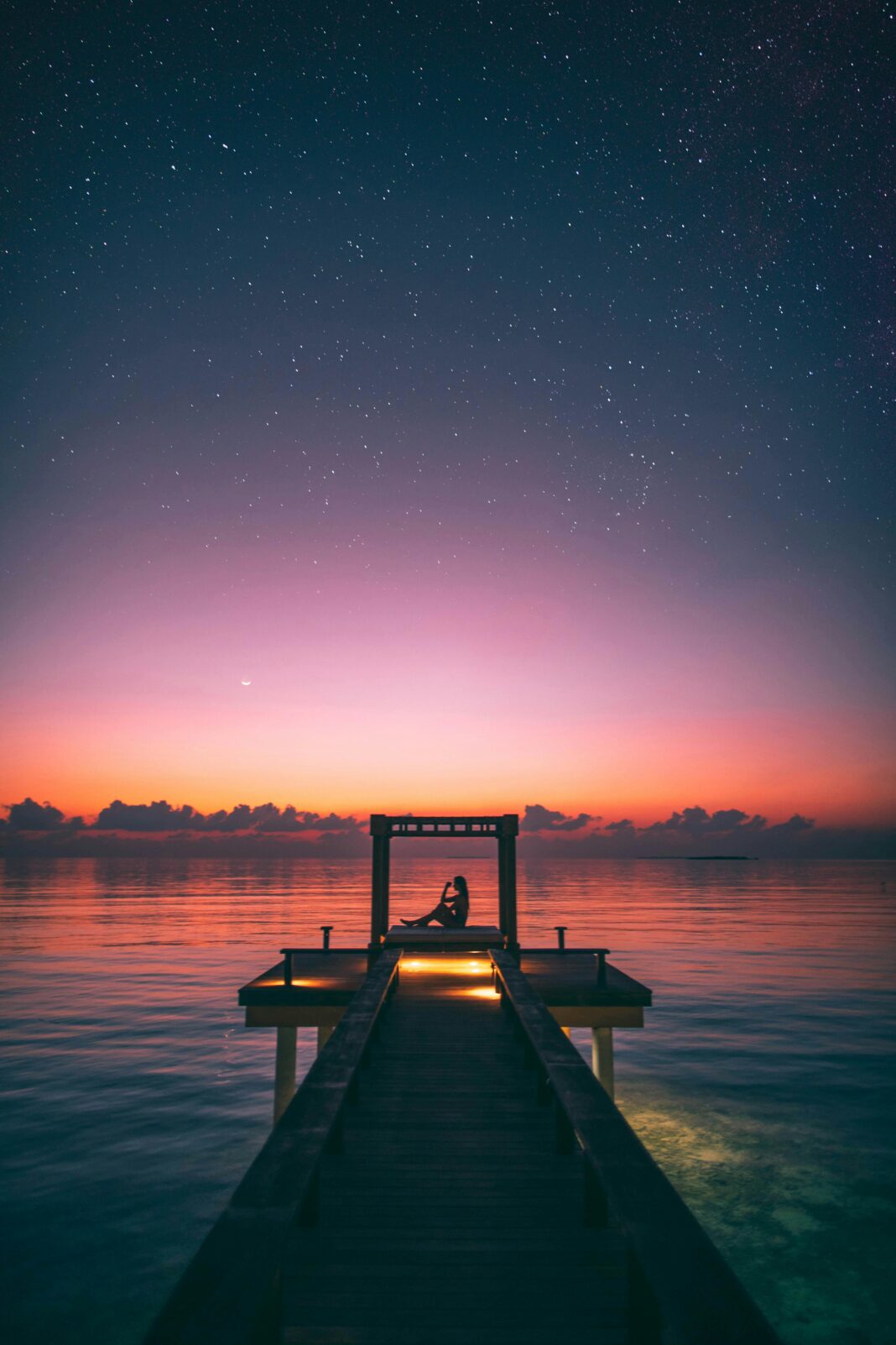 maldives Spokojna scena osoby relaksującej się na molo na Malediwach o zmierzchu pod rozgwieżdżonym niebem.