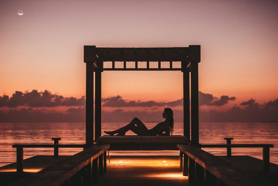 maldives Kobieta relaksuje się na przystani o zachodzie słońca na Malediwach, oferując spokojną ucieczkę.