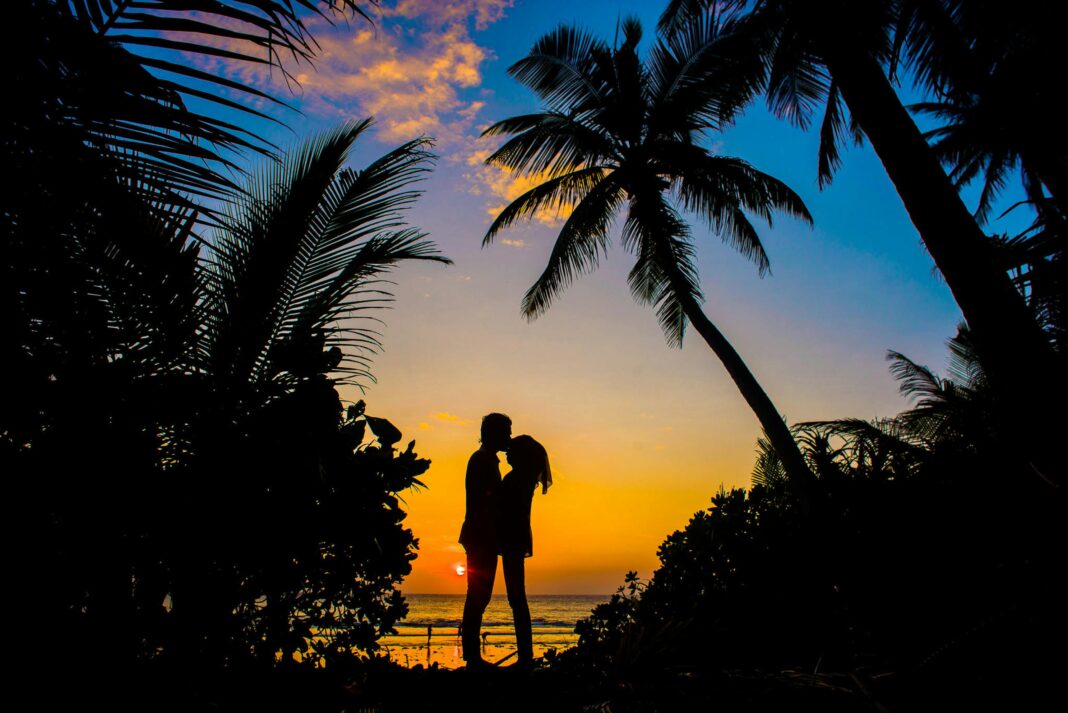 maldives Sylwetka pary spędzającej romantyczne chwile na tropikalnej plaży o zachodzie słońca z palmami.