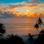 Oszałamiający tropikalny zachód słońca nad spokojnym oceanem z sylwetkami palm.