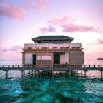 Oszałamiająca willa nad wodą o zachodzie słońca na Malediwach z tętniącym życiem niebem i turkusowymi wodami.