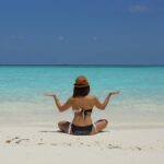 Kobieta medytująca na spokojnej plaży na Malediwach, pod czystym, błękitnym niebem.