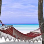 Idylliczny hamak plażowy pomiędzy palmami kokosowymi i lazurową wodą.