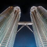Oszałamiające ujęcie pod niskim kątem kultowych wież Petronas Towers w Kuala Lumpur w Malezji, oświetlone na tle nocnego nieba.