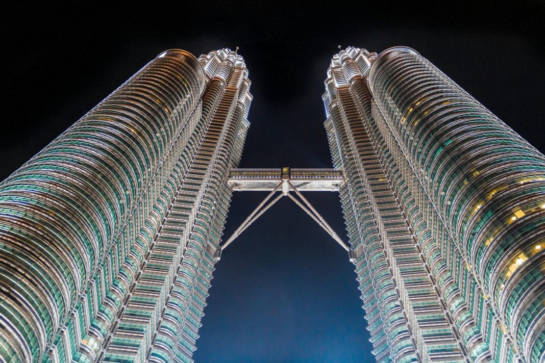 Oszałamiające ujęcie pod niskim kątem kultowych wież Petronas Towers w Kuala Lumpur w Malezji, oświetlone na tle nocnego nieba.