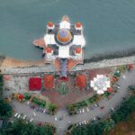 Zdjęcie lotnicze meczetu o islamskiej architekturze nad oceanem i parkingu.