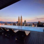 Zrelaksuj się przy luksusowym basenie bez krawędzi ze wspaniałą panoramą Kuala Lumpur i wieżami Petronas Towers o zmierzchu.