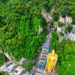 Zdjęcie lotnicze jaskiń Batu z tętniącą życiem świątynią i posągiem w gęstej zieleni.