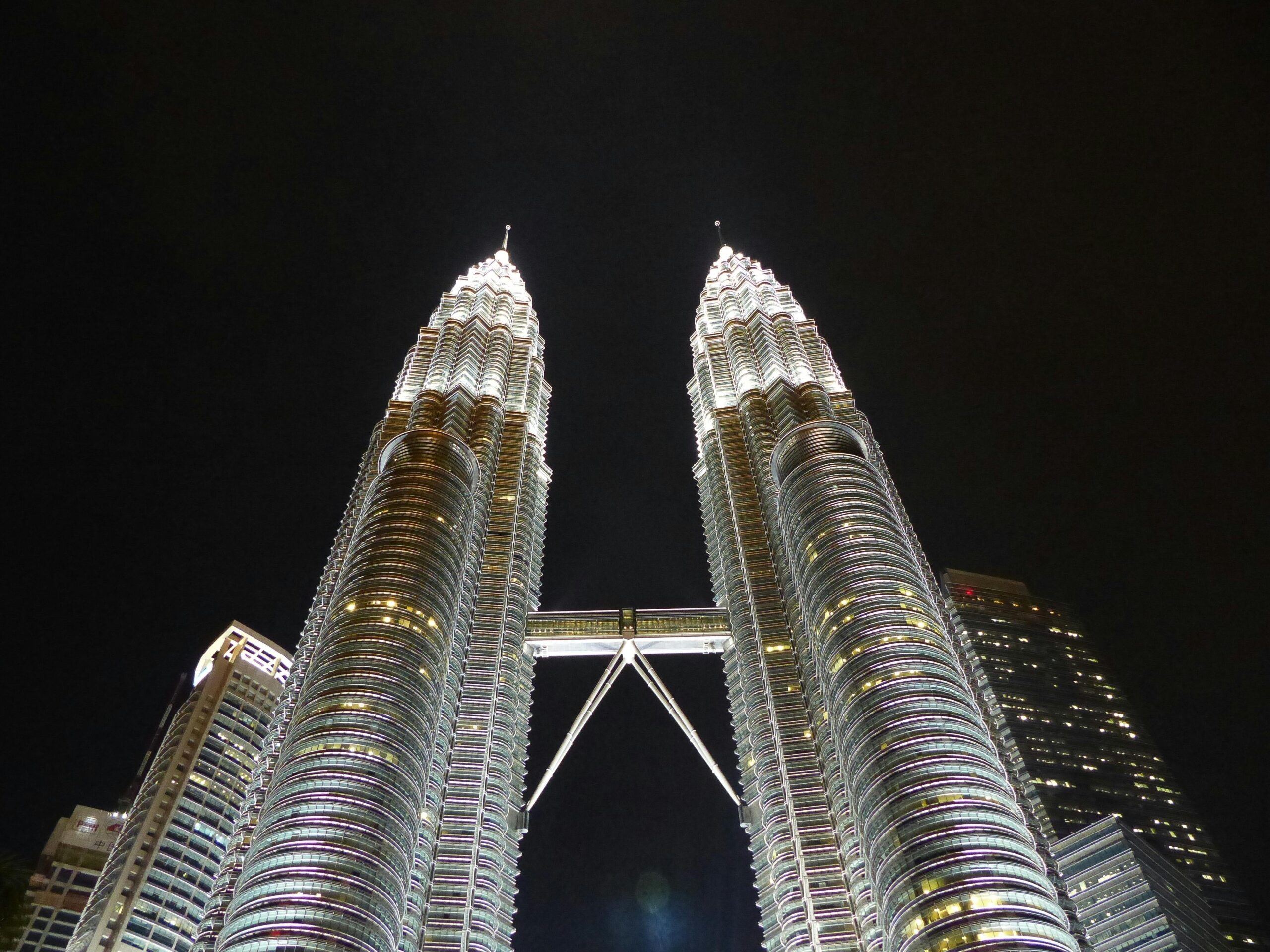 Oświetlone bliźniacze wieże Petronas na tle nocnego nieba w Kuala Lumpur, prezentujące nowoczesną architekturę.