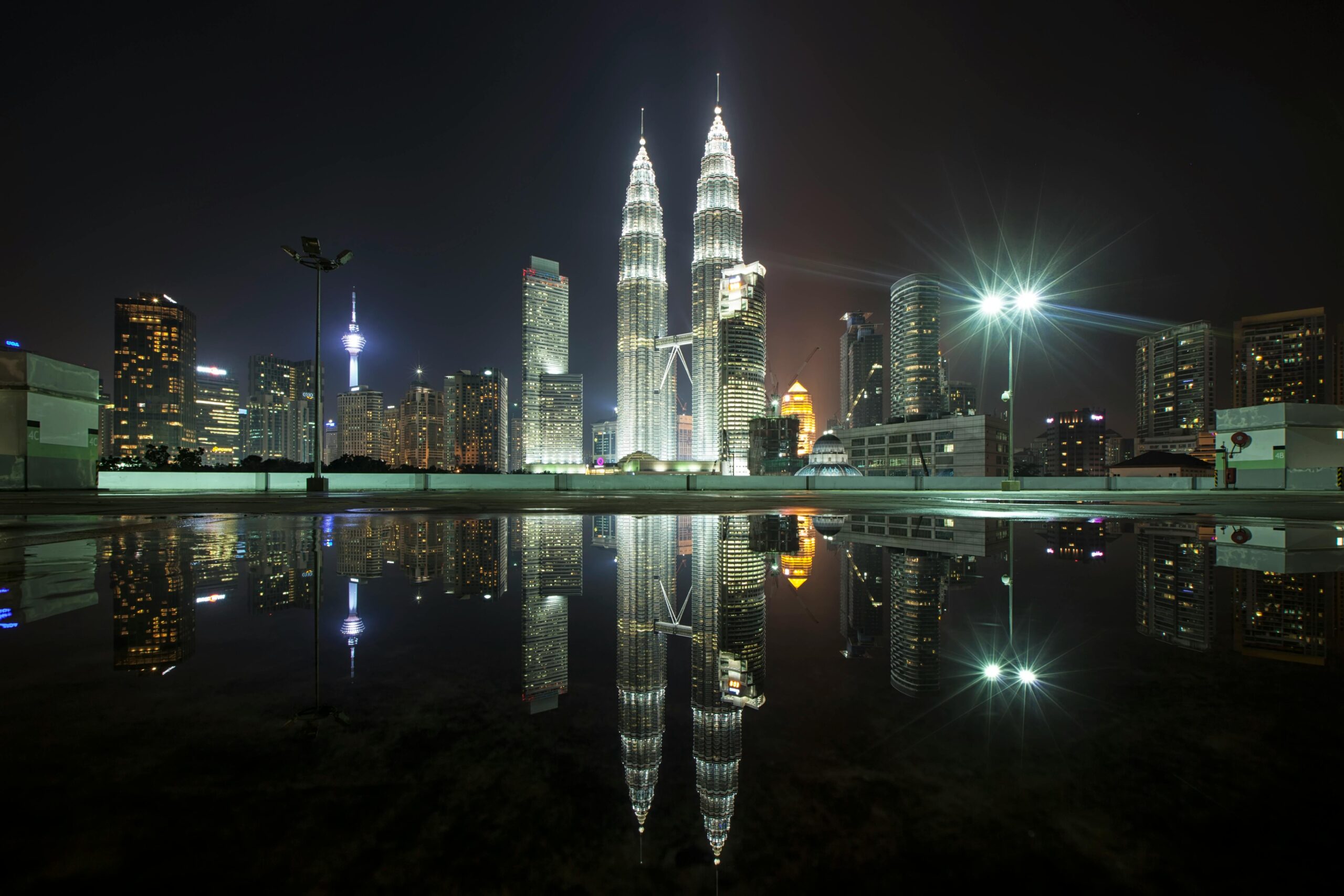 Piękny widok na panoramę Kuala Lumpur z kultowymi wieżami Petronas Towers nocą ze światłami miasta i odbiciami.