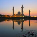 Piękny meczet odbijający się w jeziorze o zachodzie słońca, prezentujący architekturę islamską.