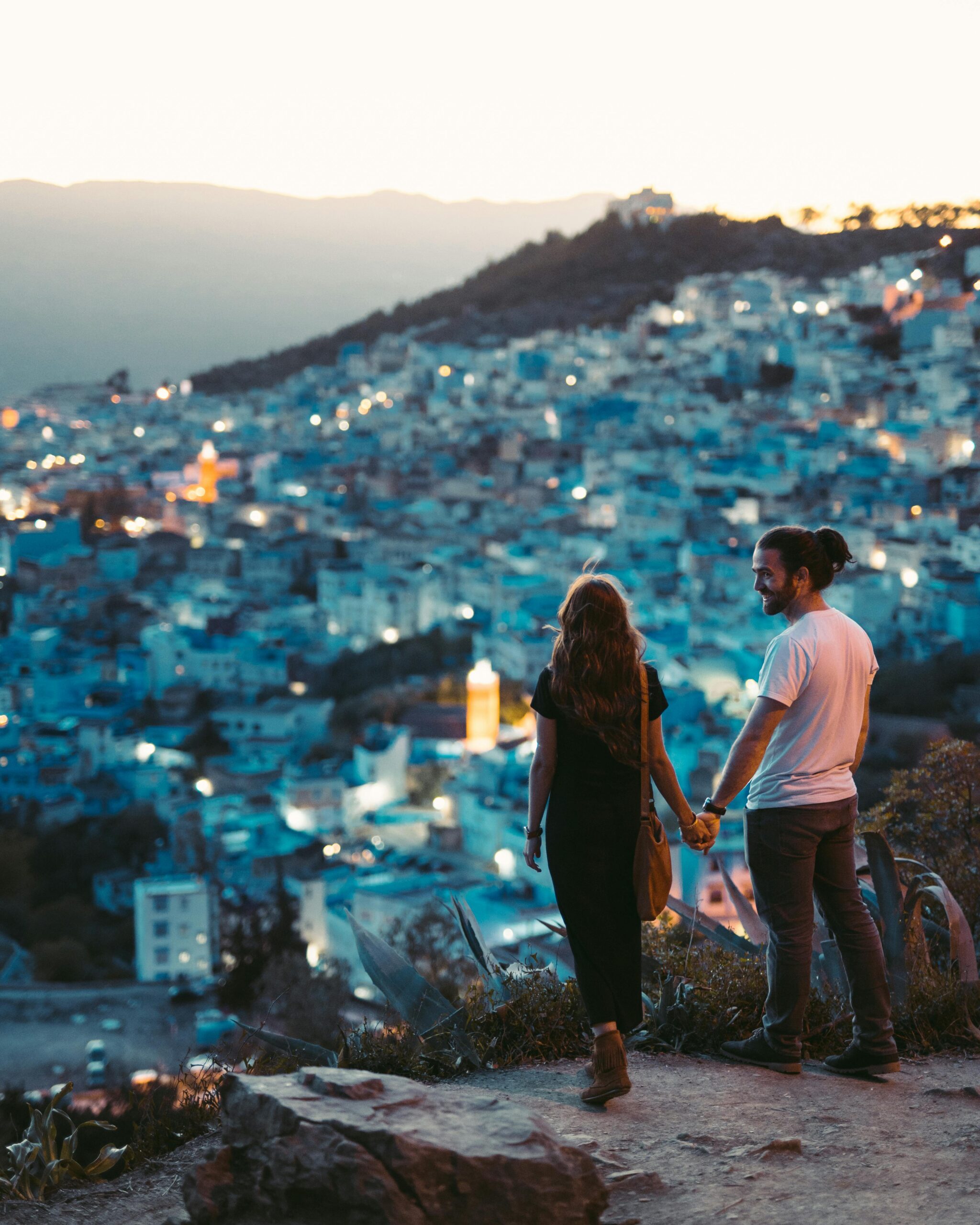 Romantyczna para trzymająca się za ręce z widokiem na Chefchaouen w Maroku o zmierzchu.