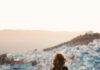 Kobieta stoi na skale, podziwiając panoramiczny widok na Chefchaouen w Maroku o zachodzie słońca.