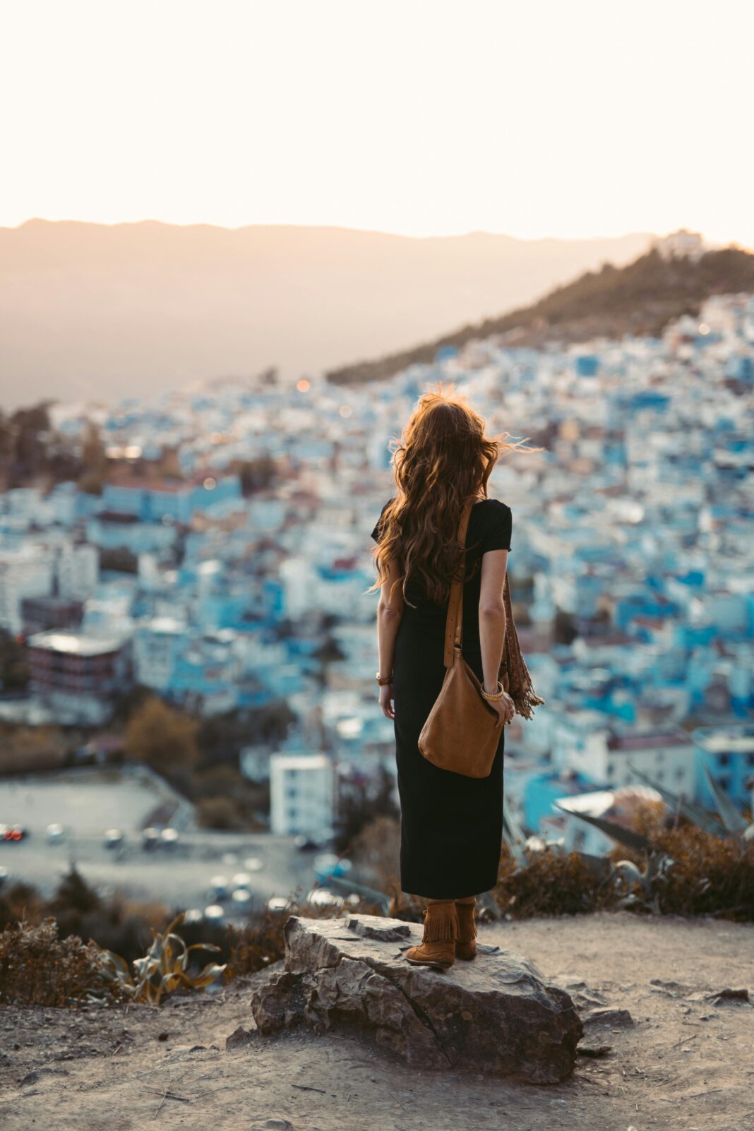 Kobieta stoi na skale, podziwiając panoramiczny widok na Chefchaouen w Maroku o zachodzie słońca.