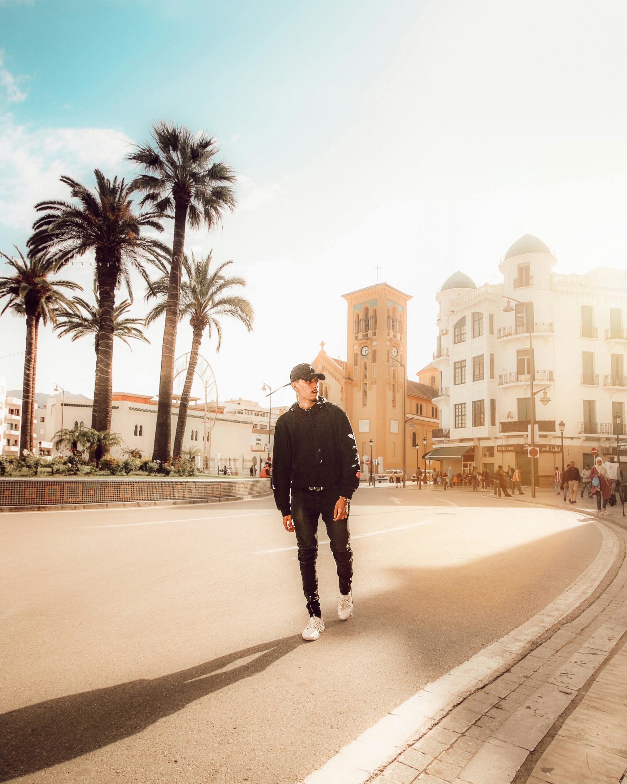 Stylowy mężczyzna idący tętniącą życiem ulicą miasta z palmami i zabytkową architekturą.