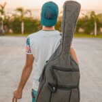 Agadir – najlepsze plaże i atrakcje turystyczne Młody mężczyzna w swobodnym stylu niosący futerał na gitarę na zewnątrz w Rabacie, Maroko.