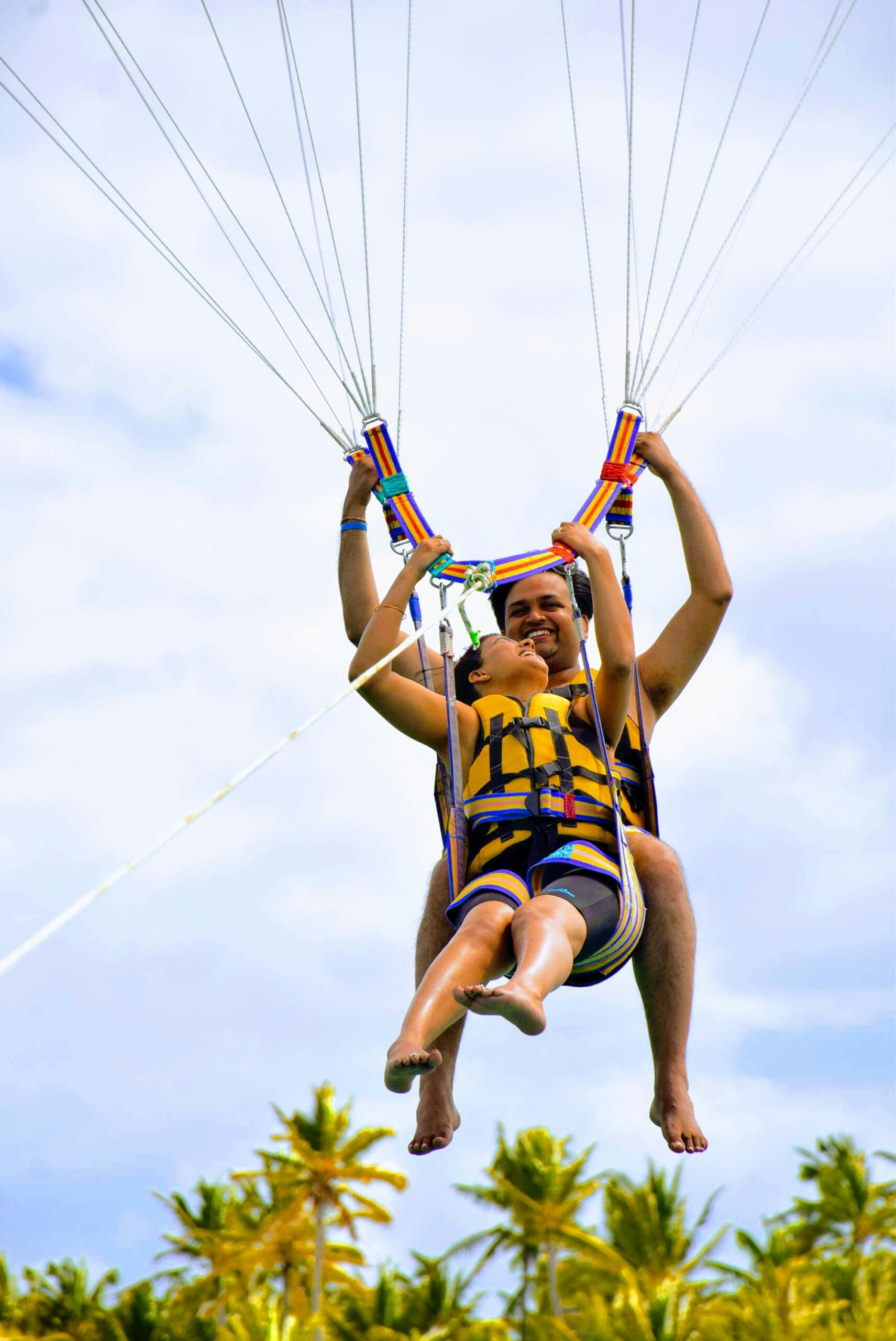 Radosna para parasailingowa nad bujnymi palmami na Mauritiusie, przeżywająca ekscytującą przygodę.