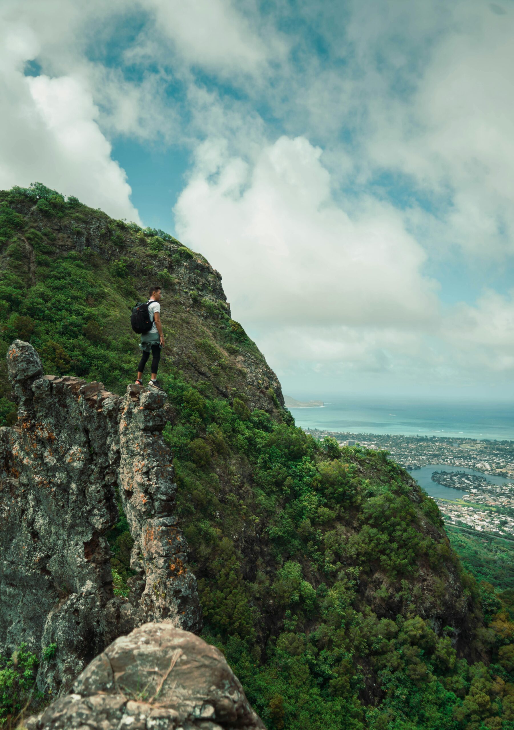 Mężczyzna stoi na skalistym zboczu góry, z widokiem na panoramę miasta i ocean, prezentując przygodę na świeżym powietrzu.