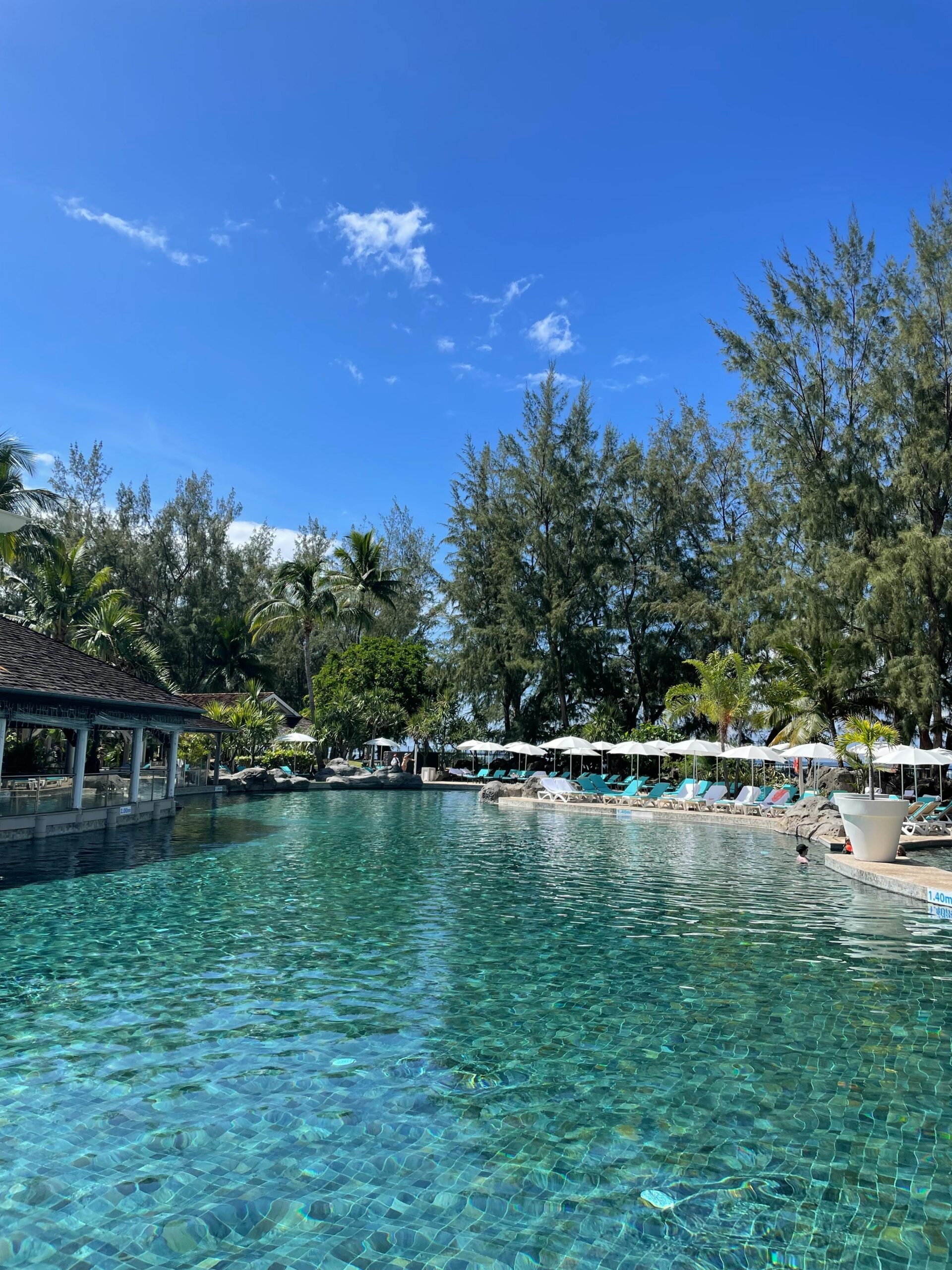 Odkryj spokojną atmosferę przy basenie w tropikalnym kurorcie z bujną zielenią i czystym, błękitnym niebem.