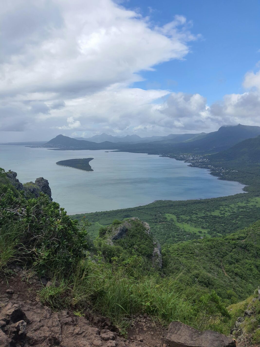 Zapierający dech w piersiach widok na nadmorski krajobraz z bujną zielenią, górami i morzem pod zachmurzonym niebem.