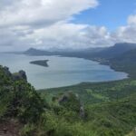 Zapierający dech w piersiach widok na nadmorski krajobraz z bujną zielenią, górami i morzem pod zachmurzonym niebem.