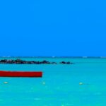 Żywa czerwona łódź unosi się na turkusowych wodach pod czystym, błękitnym niebem na Mauritiusie, tworząc spokojny krajobraz morski.