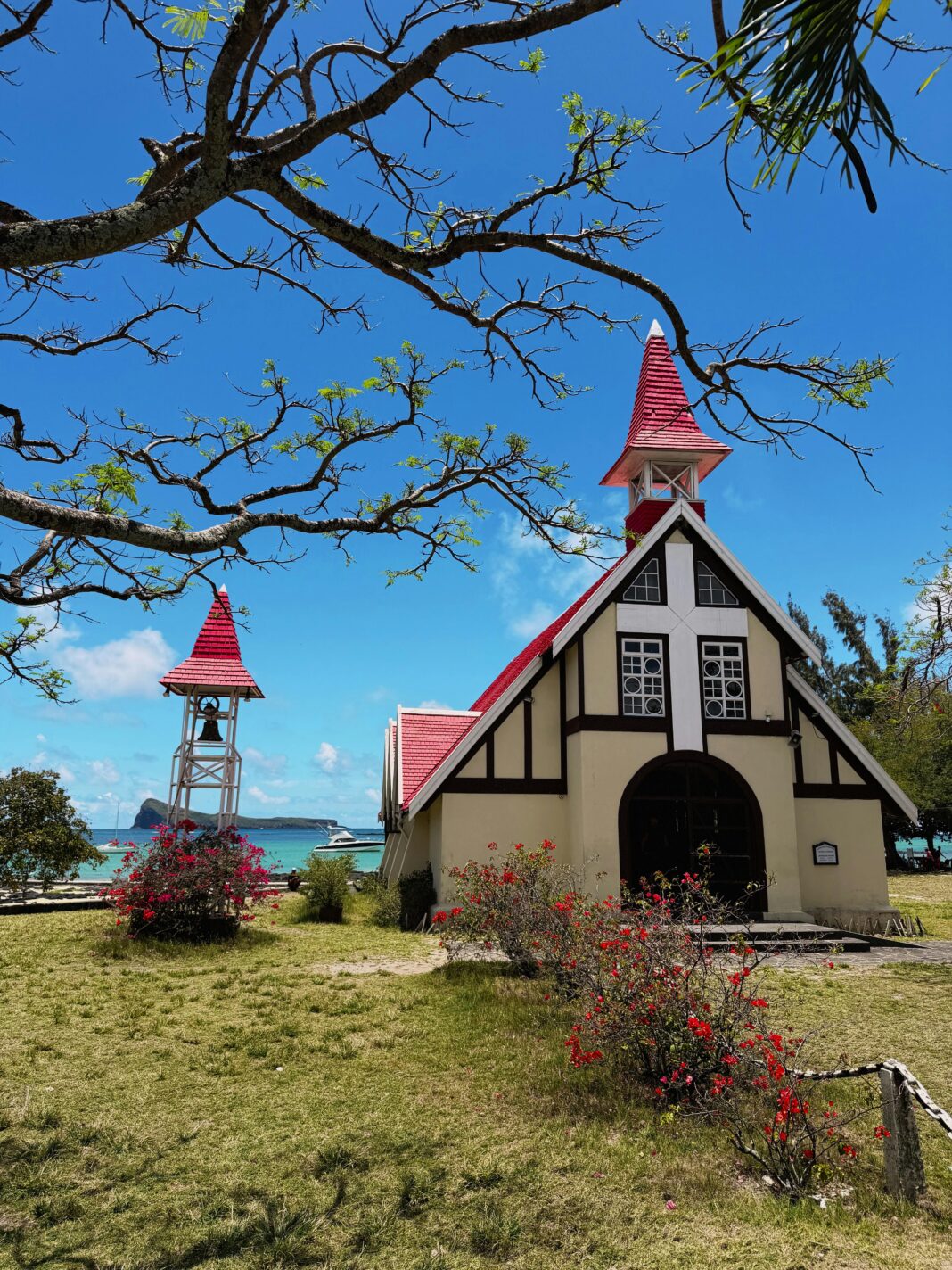 Malowniczy kościół z czerwonymi dachami nad turkusowym morzem pod czystym, błękitnym niebem.