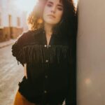 Stylowa kobieta z kręconymi włosami pozuje w złotym świetle słońca Santiago de Querétaro.