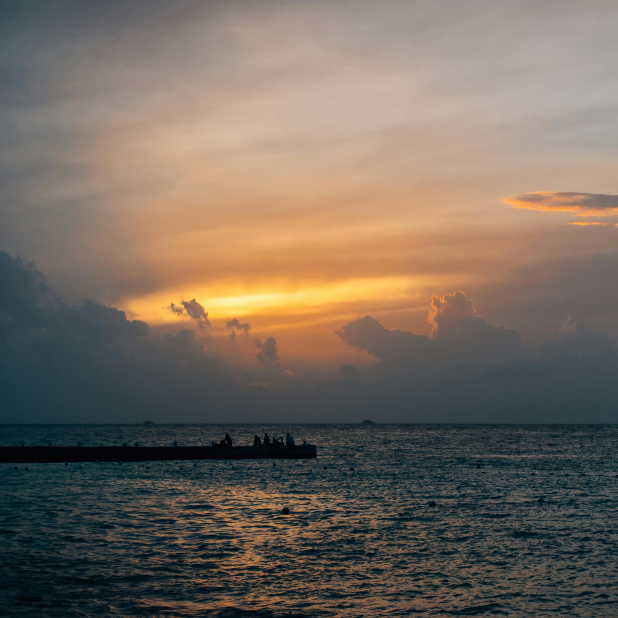 Spokojny zachód słońca z dramatycznymi chmurami nad oceanem i sylwetką molo dla uspokajającego krajobrazu morskiego.