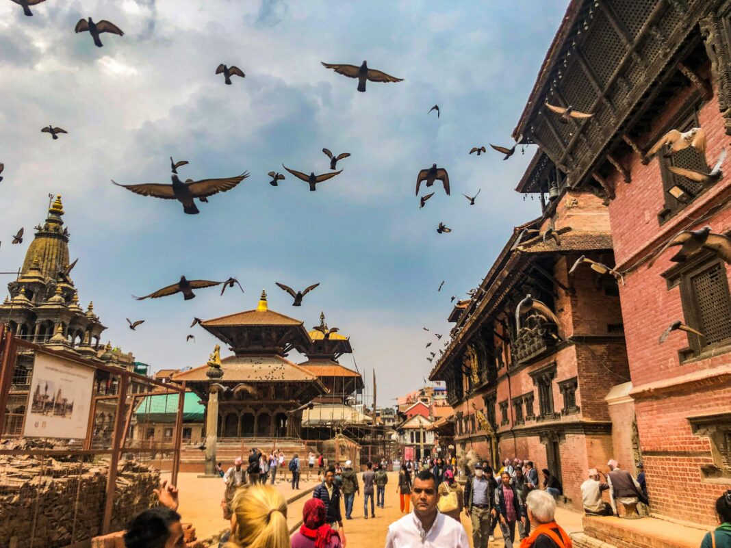 nepal Wibrująca scena na placu Patan Durbar z ludźmi, gołębiami i tradycyjną architekturą Newari pod zachmurzonym niebem.