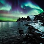 Majestatyczna zorza polarna oświetla ośnieżone wybrzeże Lenvik w Troms w Norwegii.
